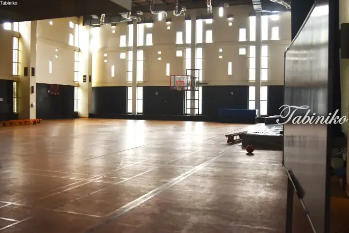 Spacious indoor basketball court with wooden flooring, high ceilings, and tall windows in a modern sports facility.