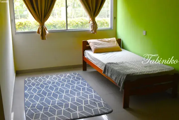 Bright bedroom with lime green walls, wooden single bed, and blue geometric rug near a window with yellow curtains.