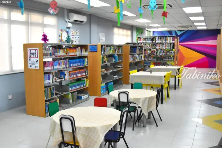 Bright school library with colorful bookshelves, reading tables, and sea-themed decorations hanging from the ceiling.