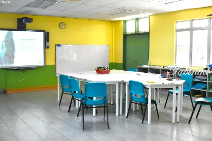 Modern classroom with yellow walls, blue chairs, and a projector screen showing an Egyptian statue.