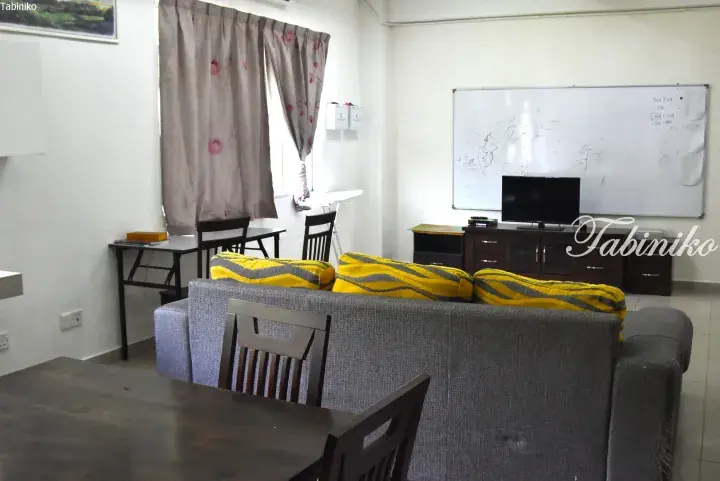 Spacious living room with grey sofa, yellow cushions, TV, whiteboard, and dining table in a Malaysian property.