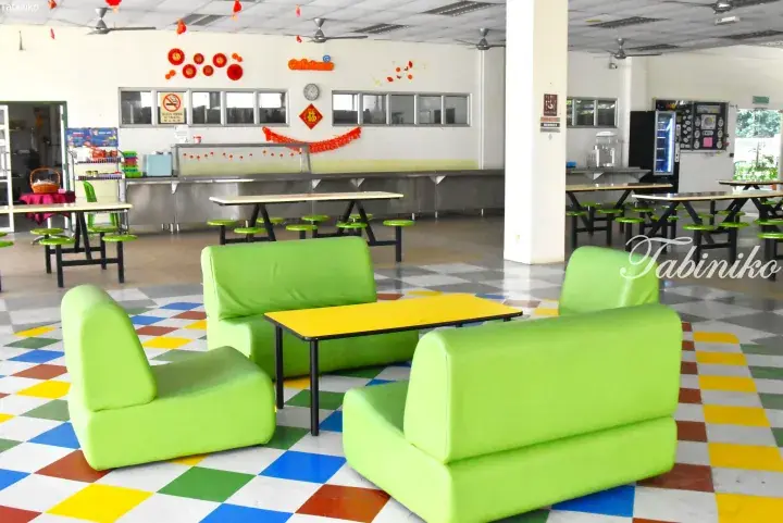 Bright school cafeteria with lime green modular sofas, yellow tables, and colorful checkered flooring.