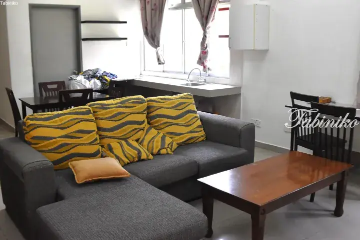 Grey L-shaped sofa with yellow patterned cushions in a modern Malaysian apartment living room.