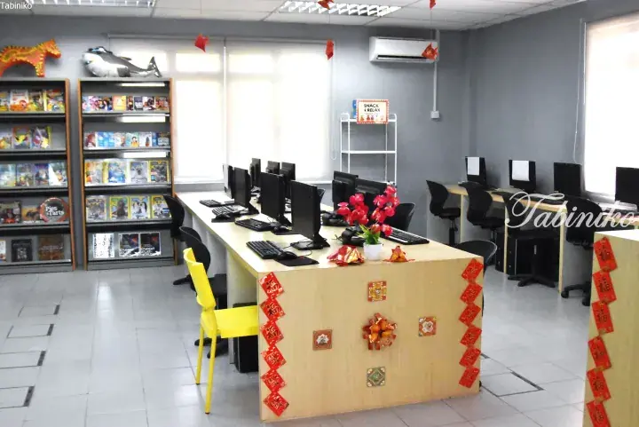 Modern computer lab with rows of PCs, bookshelves, and festive red decorations in a Malaysian study center.