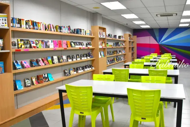 Bright library with wooden bookshelves, lime green chairs, and a colorful mural wall.