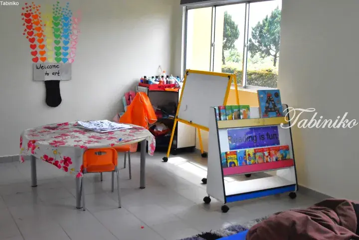 Colorful children’s art corner with heart-shaped wall art, table, easel, and bookshelf reading ‘Reading is fun.’