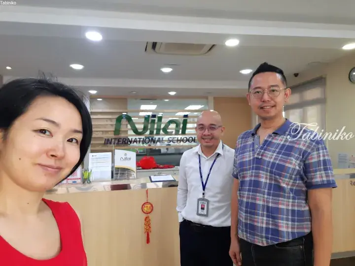 Three people smiling at the reception desk of Nilai International School in Malaysia.