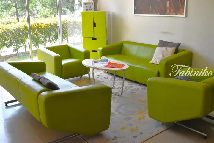 Bright green leather sofas and armchairs arranged around a coffee table in a modern lounge with large windows.