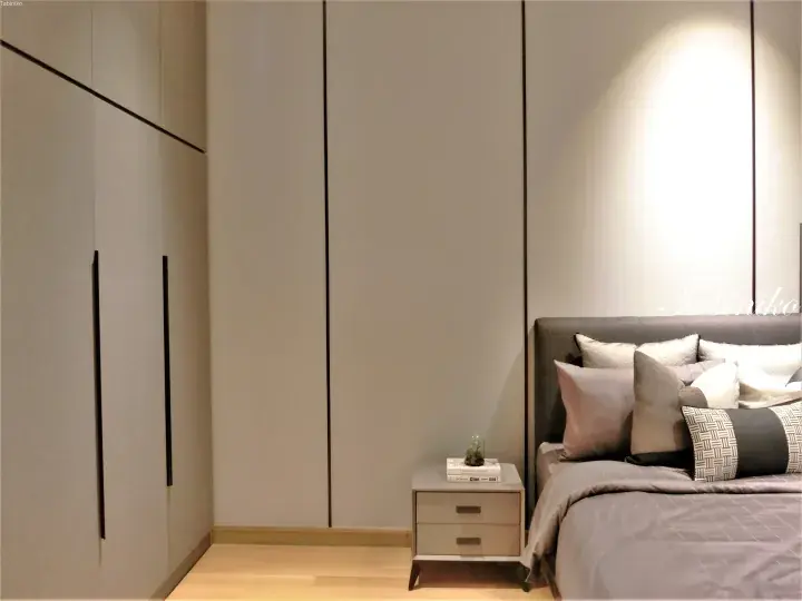 Modern bedroom interior featuring a grey upholstered bed, sleek built-in wardrobes, and a minimalist bedside table.