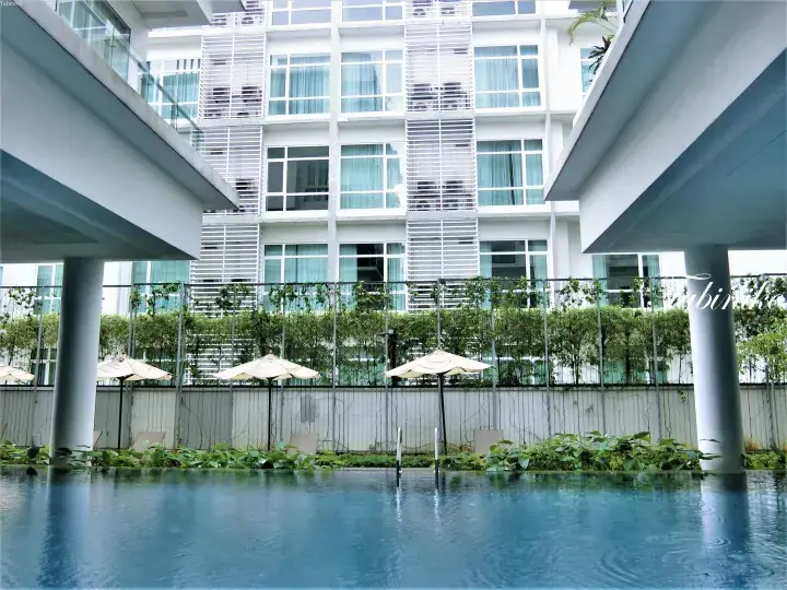 Modern hotel pool with white umbrellas and greenery, framed by white pillars and a multi-story building.