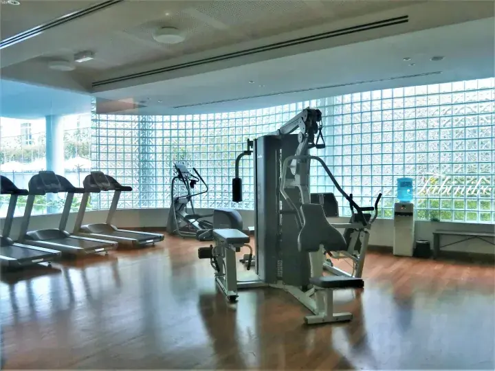 Well-lit hotel gym with treadmills, elliptical, and weight machines against a glass block wall.