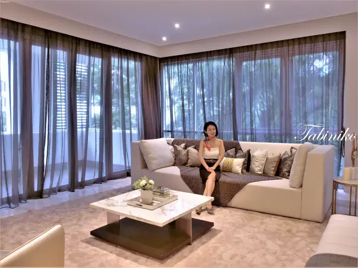 Woman sitting on a beige sofa in a modern luxury living room with floor-to-ceiling windows and marble coffee table