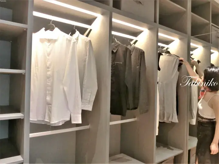 Woman organizing clothes in a modern walk-in wardrobe with integrated LED lighting and grey shelving units.