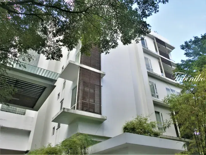 Modern white residential building with wooden slat accents and glass balconies surrounded by lush greenery.