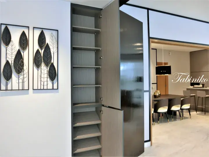 Modern interior with leaf wall art, open shelving, and a view into a dining area with a table and chairs.