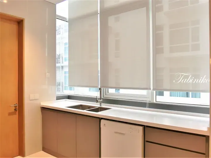 Modern kitchen with white countertops, grey cabinets, dishwasher, and roller blinds over large windows.