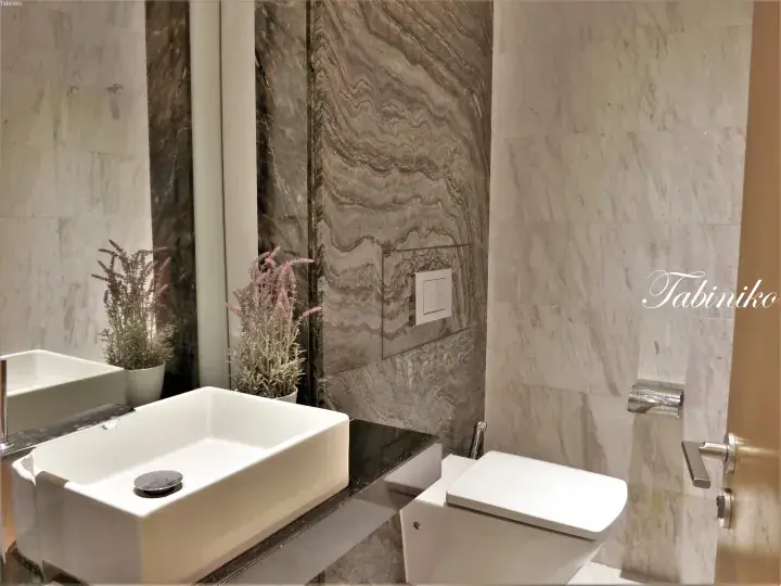 Modern luxury bathroom with marble walls, white vessel sink, and toilet.