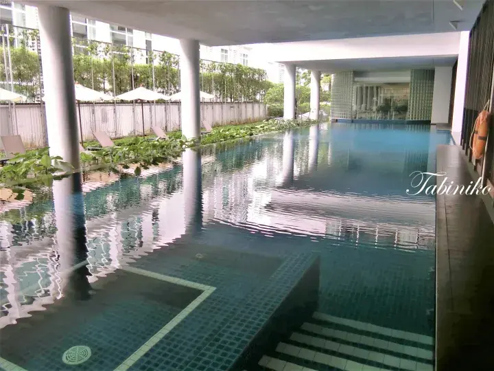 Covered swimming pool with blue tiles, lounge chairs, and greenery at a modern Malaysian property.