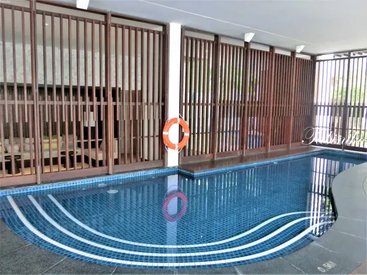 Indoor swimming pool with blue mosaic tiles, wooden slat partitions, and an orange lifebuoy at a Malaysia resort.