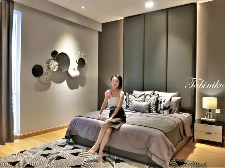 Woman sitting on a modern hotel bed with patterned pillows and a geometric rug in a stylish bedroom.