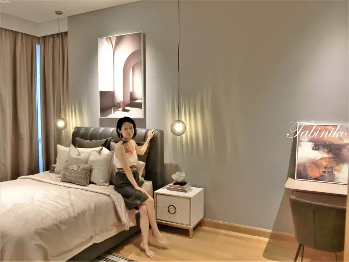 Woman sitting on a modern bed in a stylish bedroom with pendant lights and artwork.