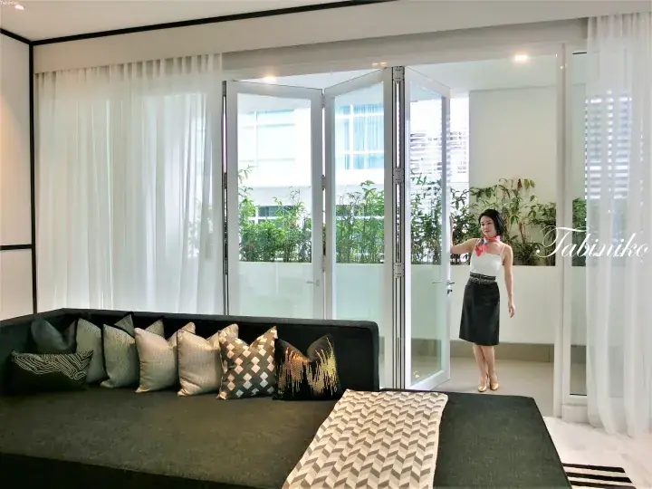 Woman standing by open folding glass doors in a modern living room with a dark sofa and balcony view