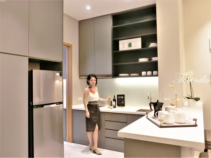 Woman in a modern kitchen with grey cabinets, stainless steel fridge, and white countertop island.