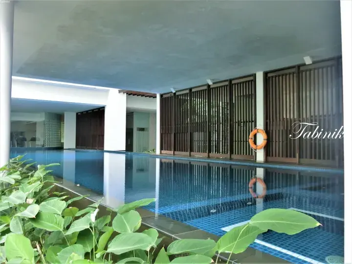 Covered swimming pool with blue tiles, wooden slat walls, and lush green plants at a Malaysia property.