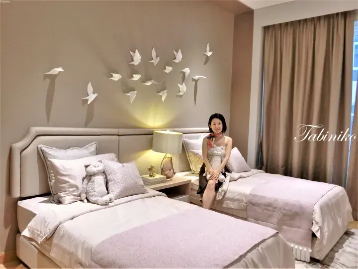 Woman sitting on a twin bed in a hotel room with bird wall art and soft lighting.