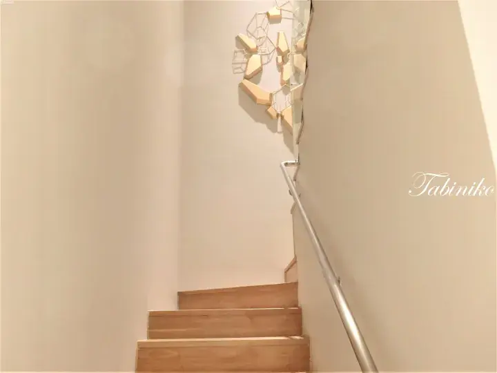 Modern wooden staircase with a geometric gold wall art installation and glass railing.