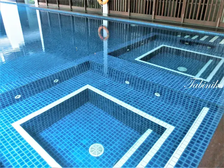 Blue mosaic tiled swimming pool with sunken seating areas and white step accents at a resort.