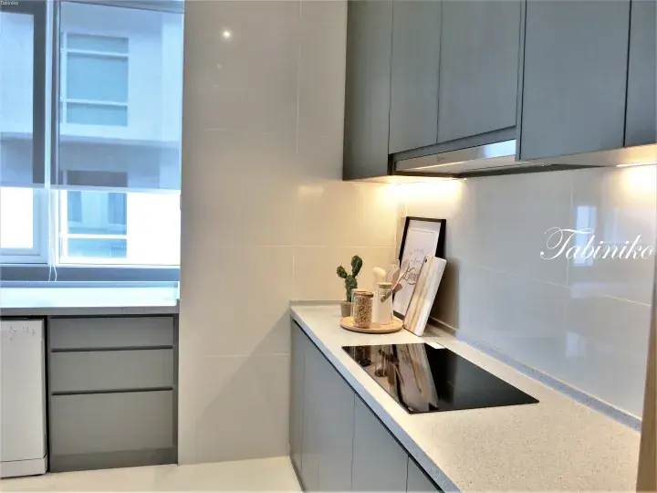 Modern grey kitchen with sleek cabinets, induction cooktop, and natural light from a window.