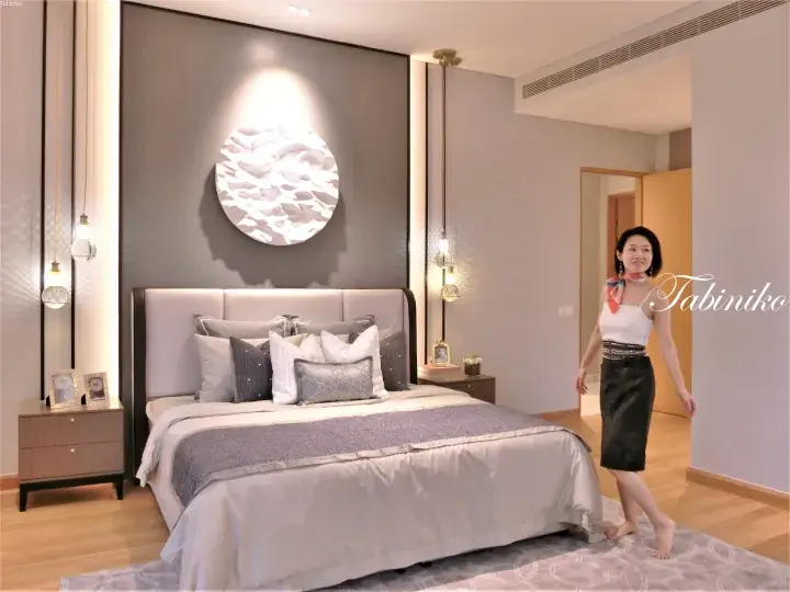 Woman in a modern luxury bedroom with a grey accent wall, moon art, and pendant lights.