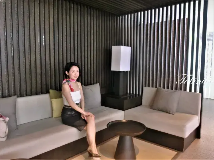Woman relaxing on a beige sofa in a modern lounge with vertical slat walls and a minimalist lamp.