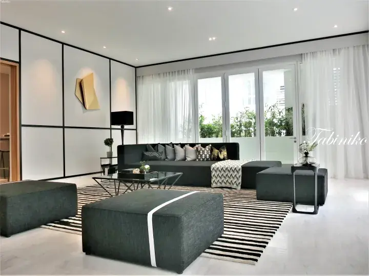 Modern luxury living room with grey sectional sofa, striped rug, and glass balcony doors in a Malaysian property.