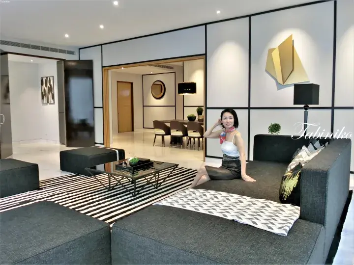 Woman sitting on a modern grey sofa in a stylish living room with a striped rug and dining area.