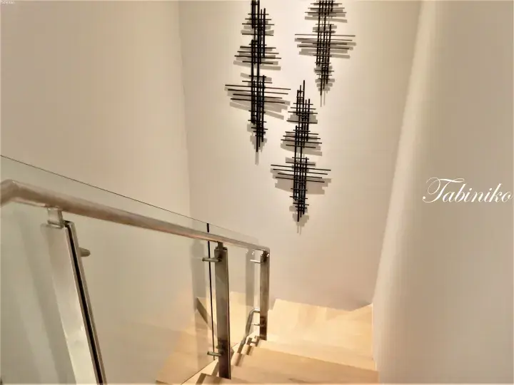 Modern staircase with glass railings and abstract black metal wall art in a minimalist interior.