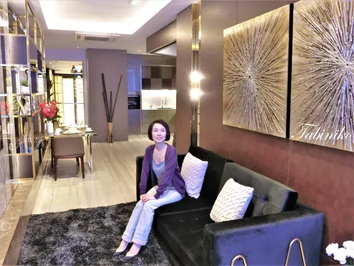 Woman sitting on a black sofa in a modern luxury apartment with gold wall art and marble flooring.