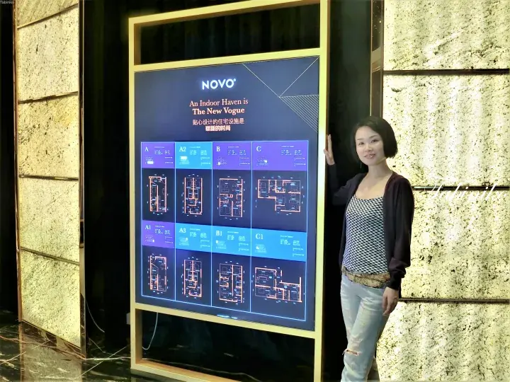 Woman standing beside a display board showing NOVO property floor plans and unit types.