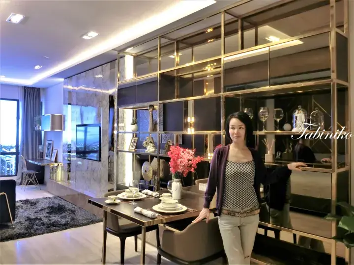 Woman standing in a modern luxury apartment dining area with a mirrored partition and marble TV wall.