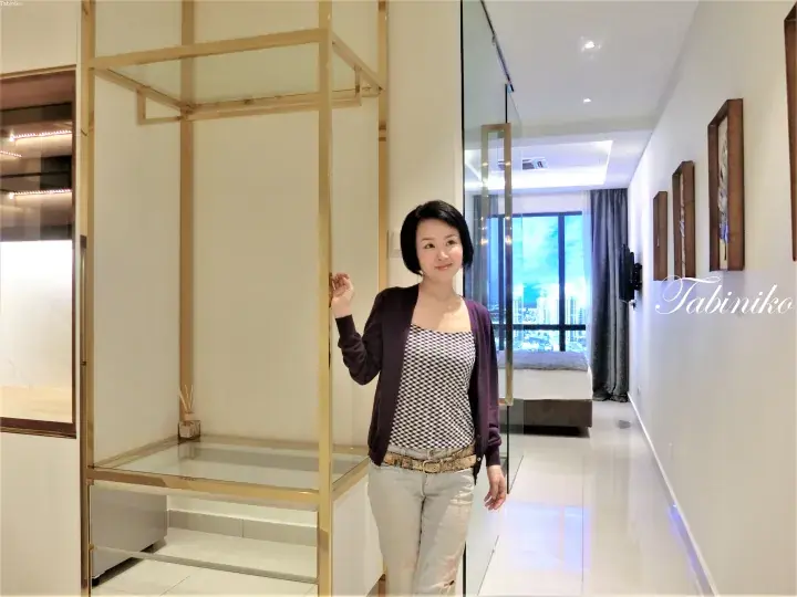 Woman standing in a modern apartment hallway with gold-framed glass partitions and a view of the city skyline.