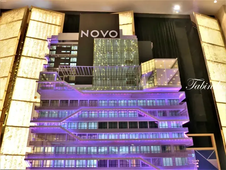 Architectural model of the NOVO building showcasing its modern design with purple accent lighting and glass facades.