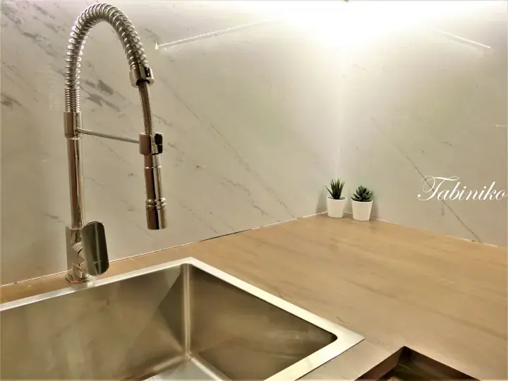 Modern kitchen sink with a pull-down faucet, marble backsplash, and wooden countertop.