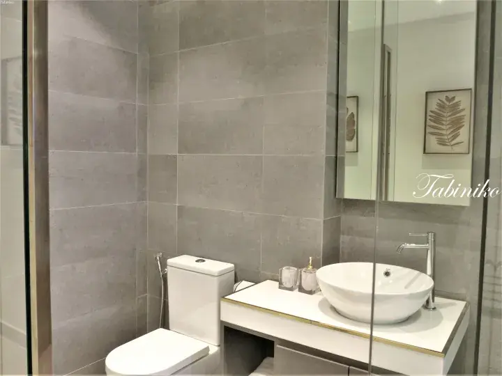Modern bathroom with grey tiles, white vessel sink, and gold accents in a Malaysian property