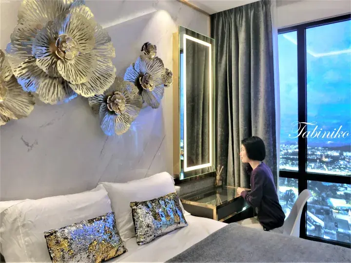 Woman admiring night city view from luxury hotel room with floral wall art and vanity mirror.