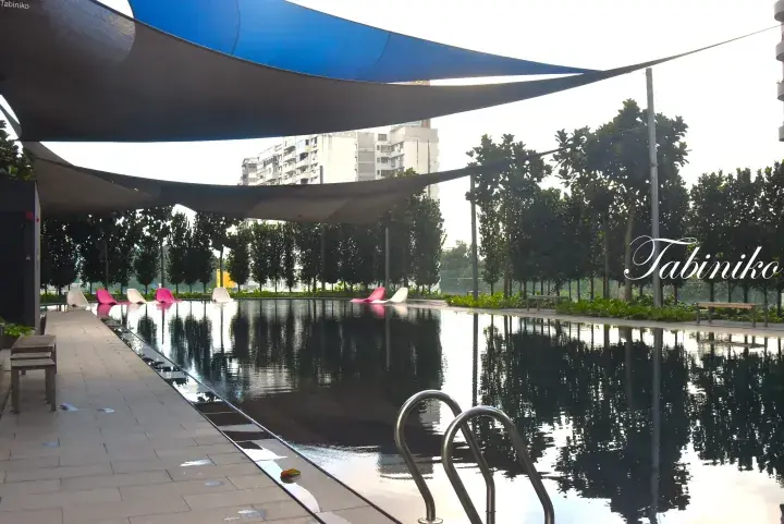 青いシェードセイルと緑豊かな庭園が特徴の、マレーシアの宿泊施設にある静かなインフィニティプール。