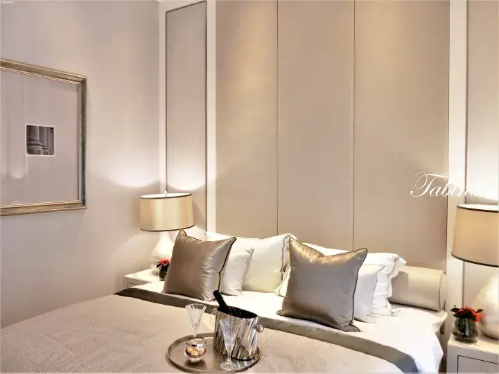 Luxury hotel bedroom with champagne on ice, plush pillows, and modern beige decor.