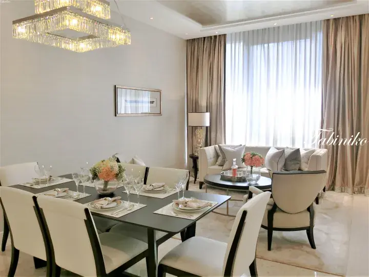 Elegant dining and living area with a crystal chandelier, set table, and beige sofa in a luxury apartment.