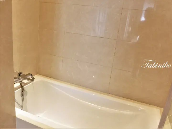 Modern bathroom featuring a white bathtub with chrome fixtures against beige tiled walls