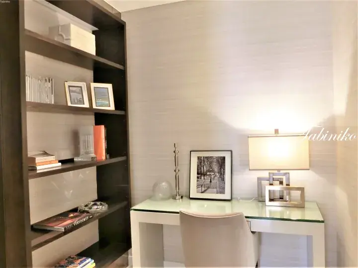 Modern home office with a glass desk, bookshelf, and lamp in a well-lit room.